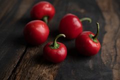 Five whole red cherry peppers with green stems on a dark rustic wooden table