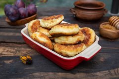 fried cottage cheese pancakes in a red dish with plums and honey on rustic wood