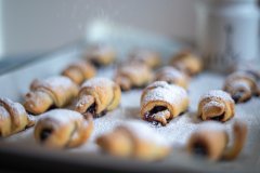 Homemade jam-filled rugelach pastries dusted with powdered sugar on a rustic tray, dark moody food photography