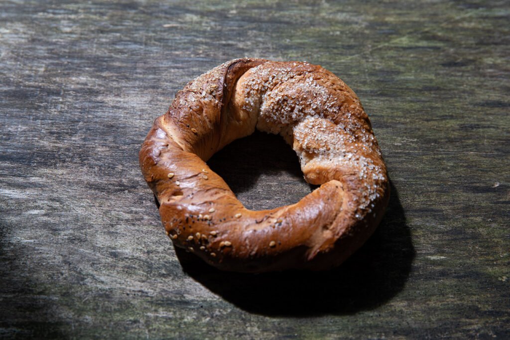 Rustic Polish obwarzanek with salt crystals on weathered grey wood, dark moody food photography